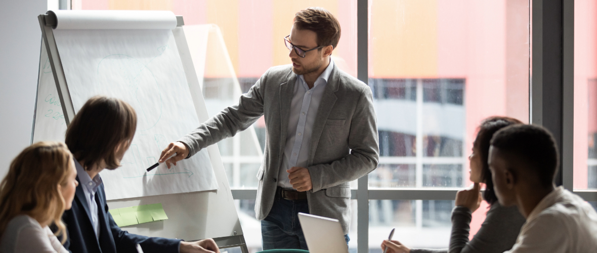 Man pointing to posterboard in front of a group of people in a conference room.