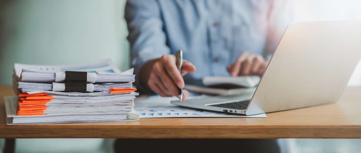 Person working at a desk with a laptop and a stack of documents clipped together.