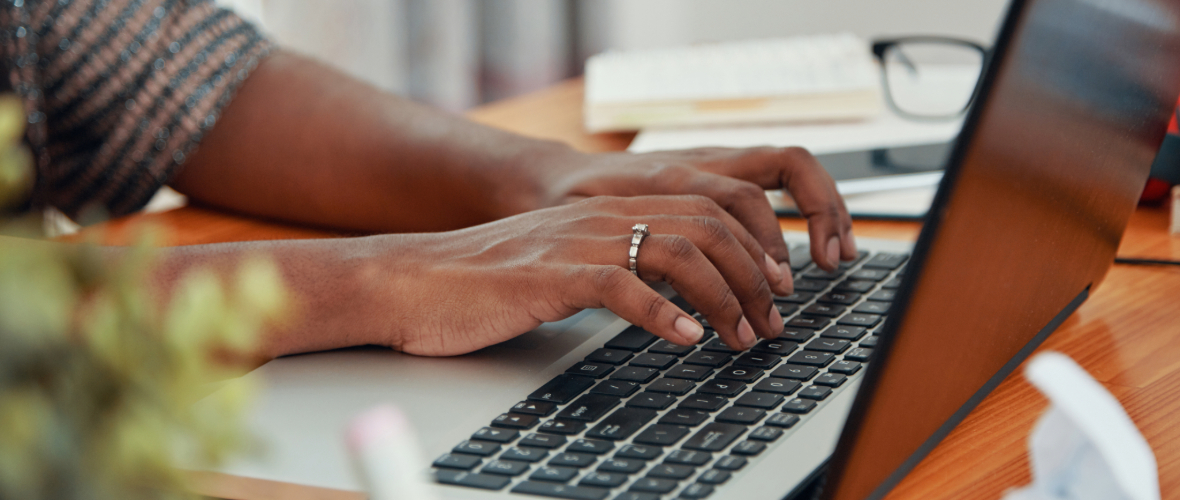 Close-up of hands typing on laptop sitting at an office desk. 