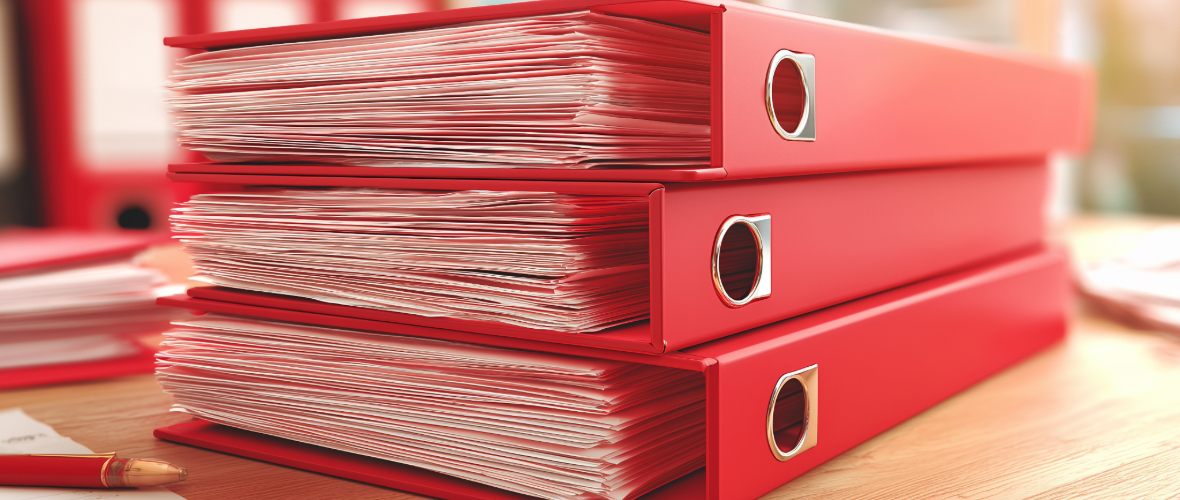 Three red binders staked on a desk.
