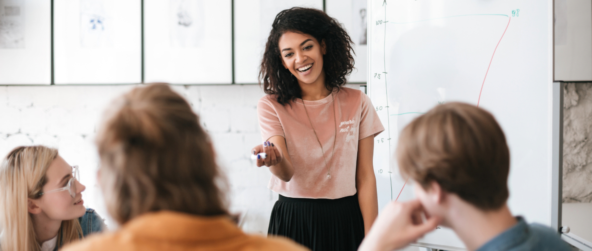 Woman presenting in front of a whiteboard to a group of people.