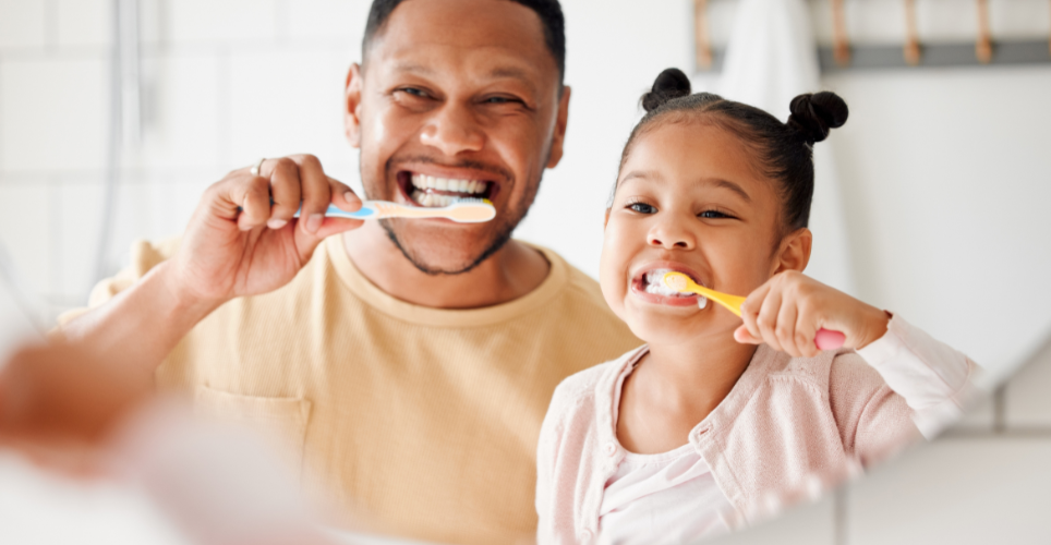 Dad and daughter looking into a mirror brushing their teeth