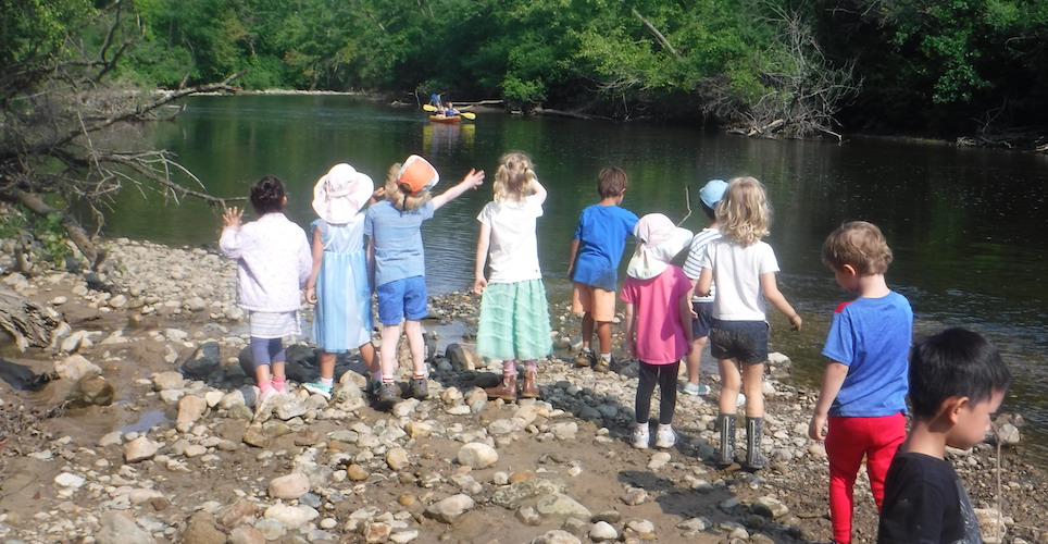 Summer day with children on the bank of the Huron River in the Arb waving the kayakers.