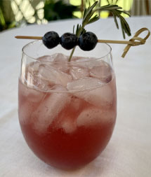 Blueberry Rosemary Spritz in a glass with ice and a rosemary sprig and 3 blueberries as garnish