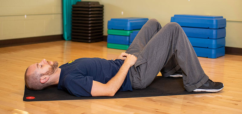 Young man laying on floor showing bridge hip raise start movement
