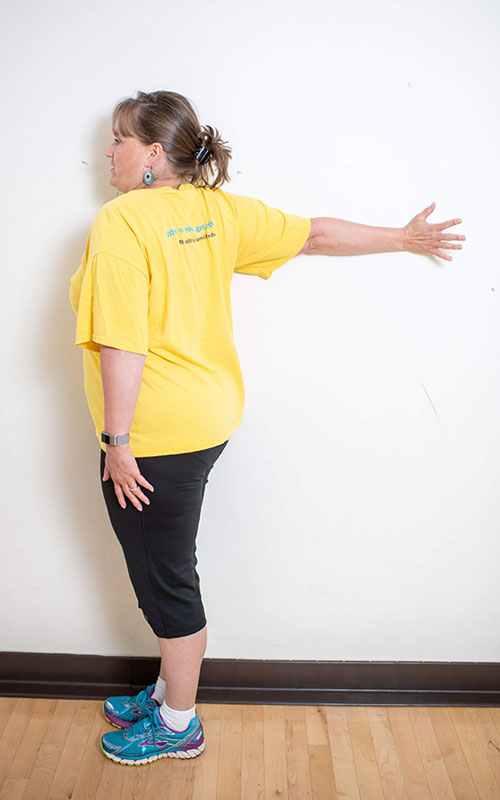 woman standing with face towards the wall showing chest and upper extremity stretch end movement