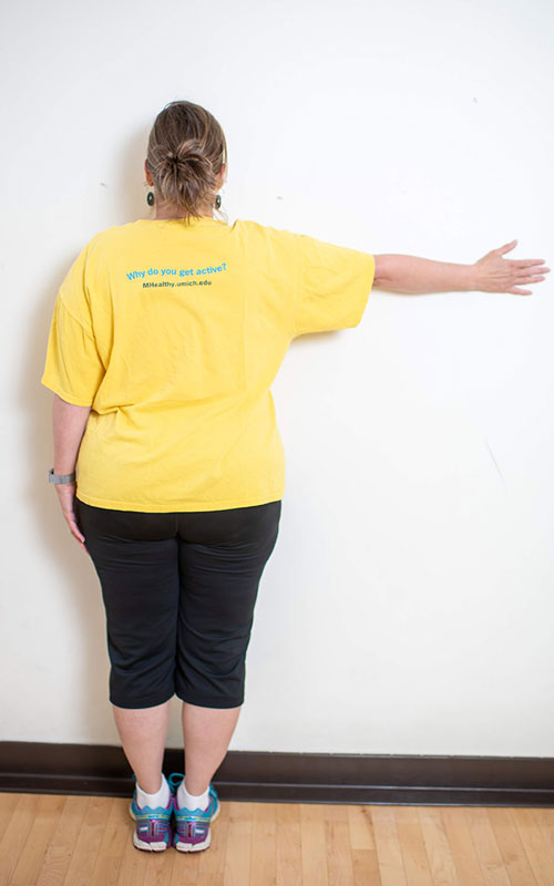 woman standing with face towards the wall showing chest and upper extremity stretch start movement