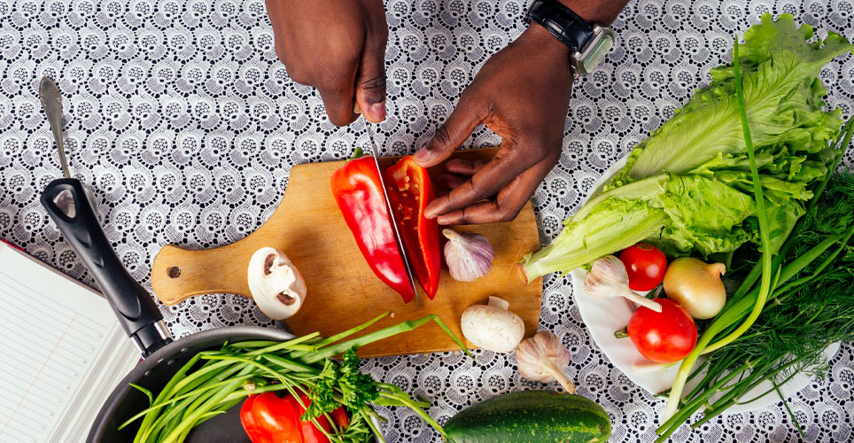 close up of two Black, female hands cutting red peppers, greens and other veggies on a cutting board