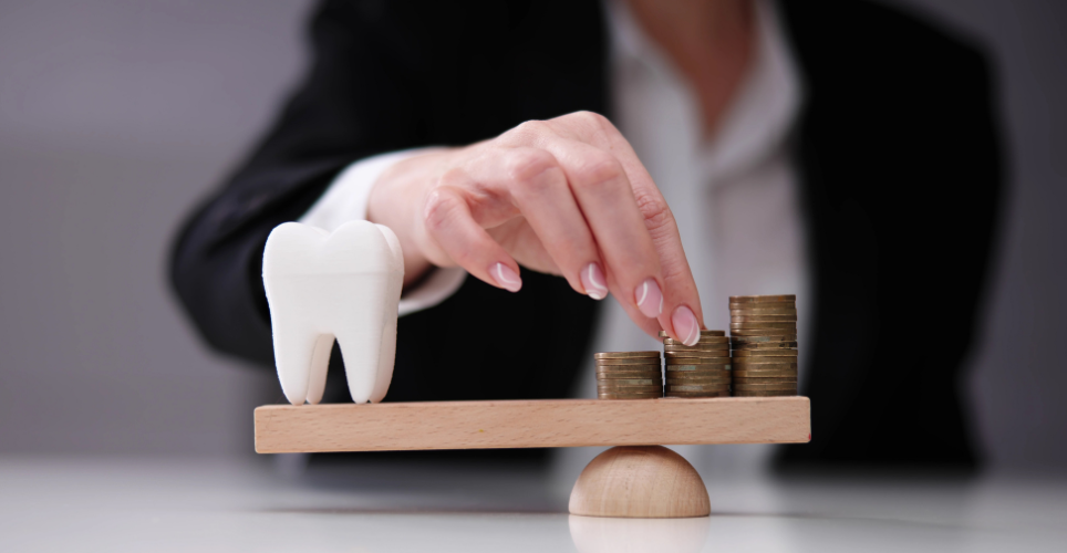 A person balancing a large model tooth and stacks of coins on a seesaw, symbolizing the cost of dental care.
