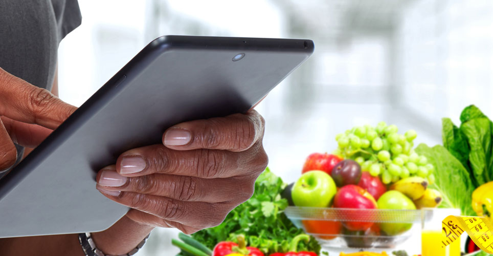 Close up of an Black woman looking into an iPad with colorful fruits and veggies in the background