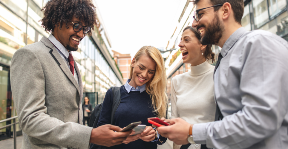 Group of four individuals sharing a joyful moment while looking at smartphones in a city street