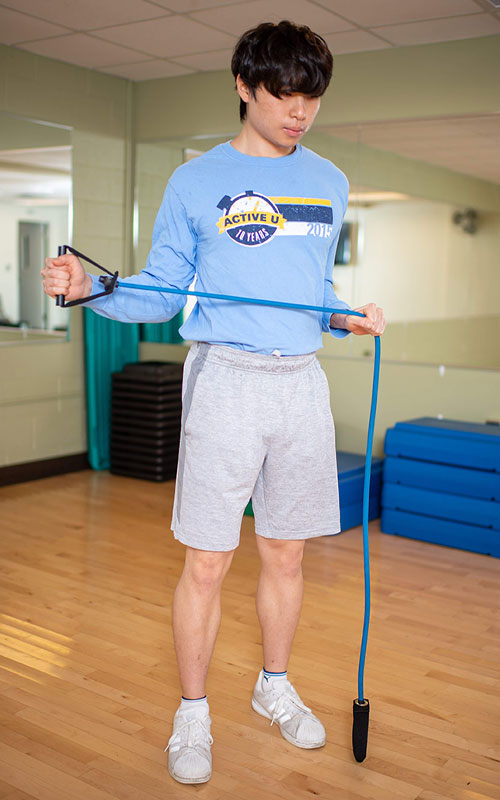 young man standing holding an exercise band showing external rotation end movement
