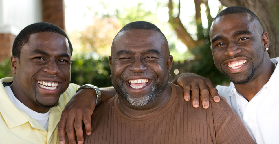 Close up of 3 African-American men with black hair and brown eyes smiling, all representing a different generation