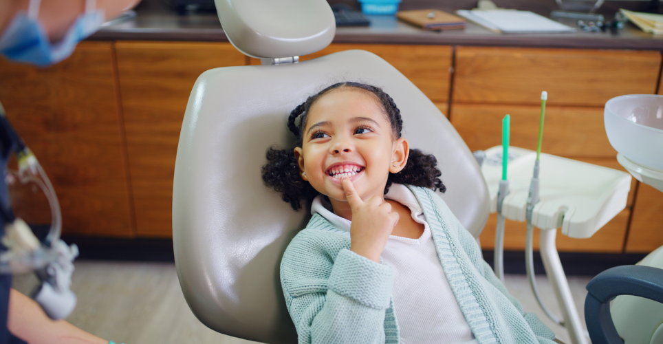 Child sitting in a dentist chair pointing to their teeth
