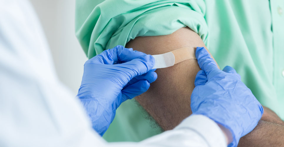 gloved hands applying a bandaid to someone arm after getting a flu shot