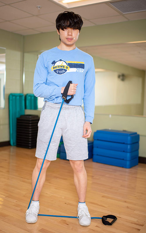 Young man standing on a exercise band holding one end in his hand showing intern rotation end movement