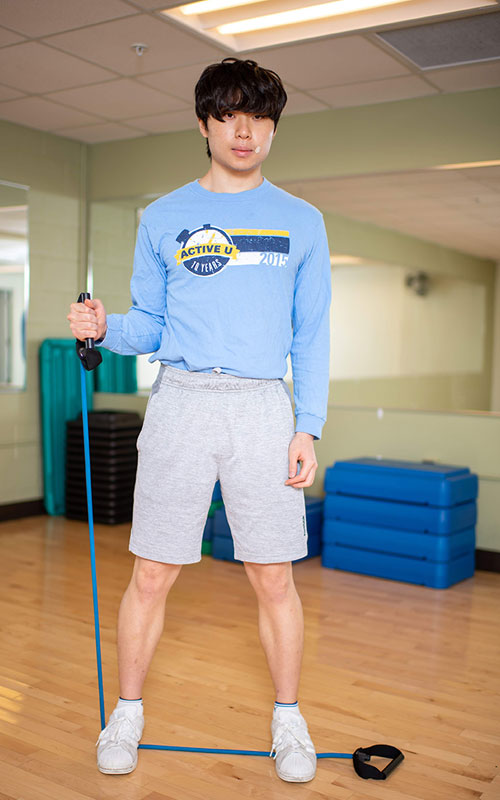Young man standing on a exercise band holding one end in his hand showing intern rotation start movement