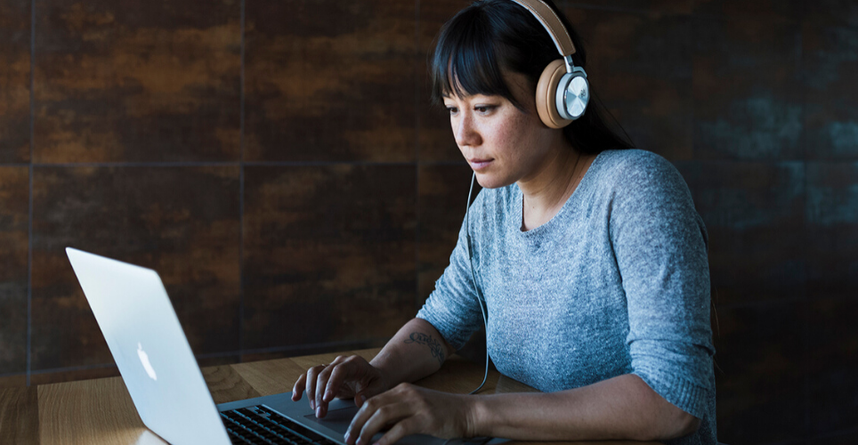 Woman wearing headphones working on a laptop at a desk