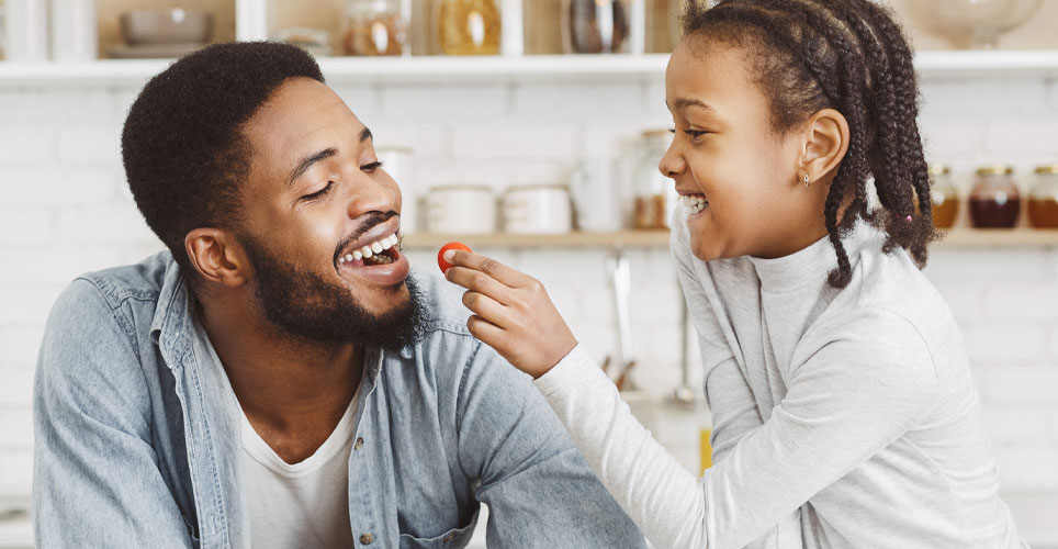 African-American man being fed a berry by his African-American daughter.