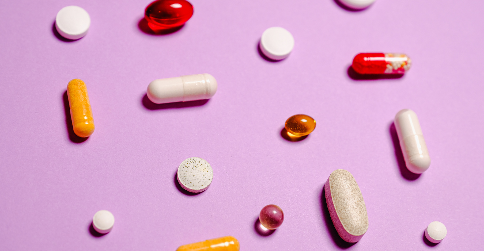 Colorful pills of different shapes on a bright pink background.