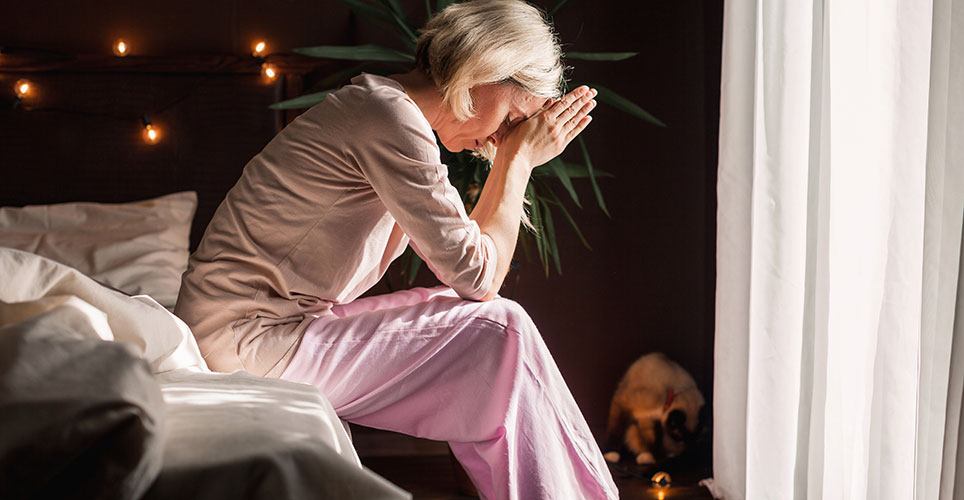 White woman with head in hands and sitting on a bed