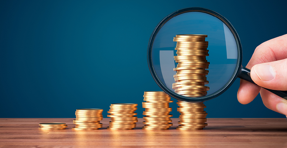 a hand holding a magnifying glass up to a stacks of coins