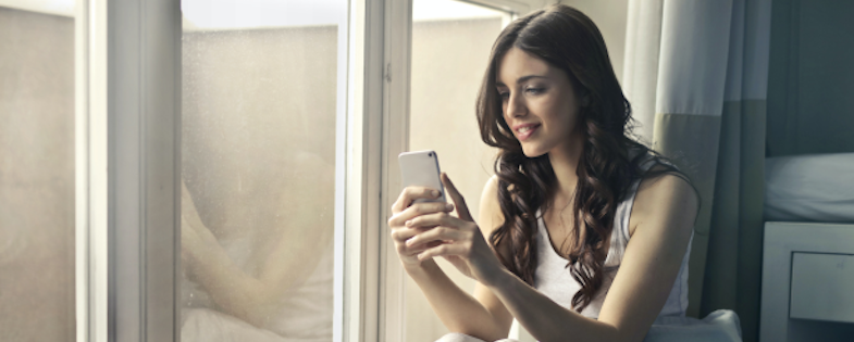 Woman looking at mobile phone sitting by window.