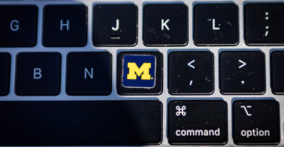 Close up of a keyboard with a University of Michigan sticker over the "M" key