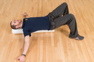 Photo of a man laying on a foam roller on the floor with arms outstretched and knees bent