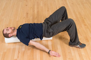 photo of man laying on a foam roller on the floor with arms outstretched and knees bent