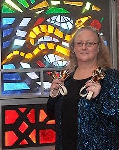 Ellen Woodard holding bells while standing in front of stained glass windows