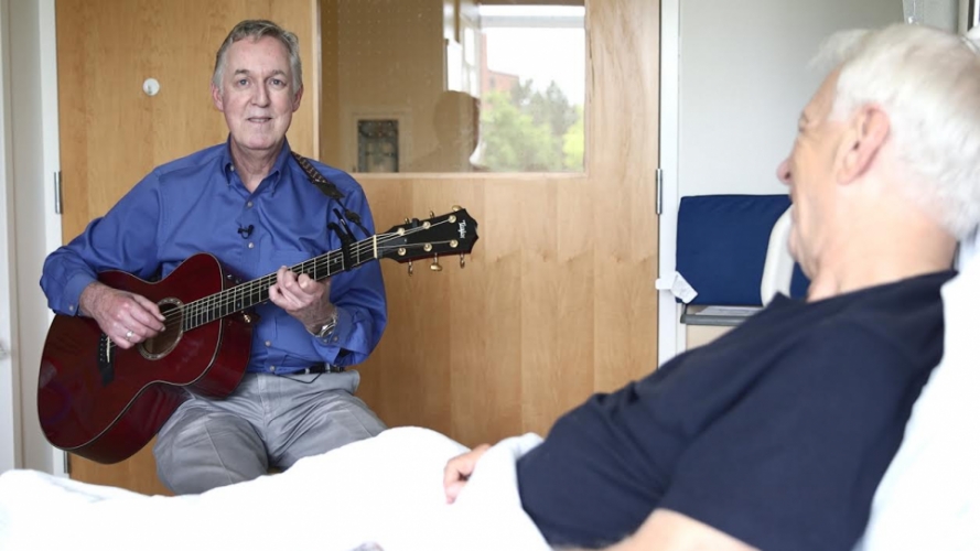 Greg Maxwell playing guitar for a hospital patient