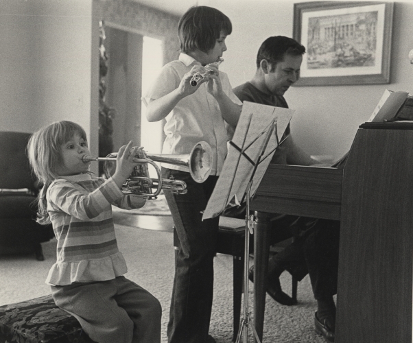Dick Kennedy seated at the piano making music with two others