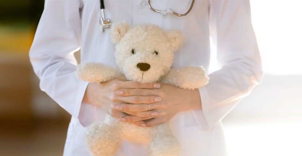 close up a Caucasian person in a white doctor's coat with a stethoscope holding a teddy bear.