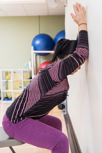 Photo of woman sitting at the edge of a chair with arms and forehead on the wall