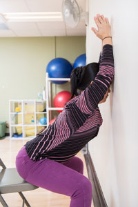 Photo of woman sitting at the edge of a chair with arms and forehead on the wall