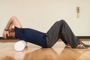 Photo of a man laying on a foam roller with hand on their head and knees bent