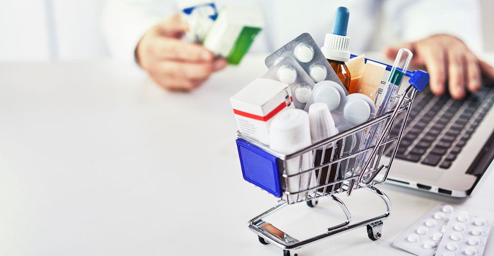 close up of a mini shopping cart filled with over the counter medication on a counter with a laptop