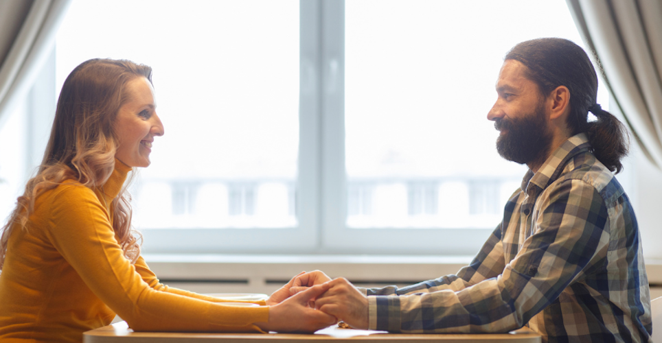 profile of a man and woman looking at one another across a table and holding each others hands. 