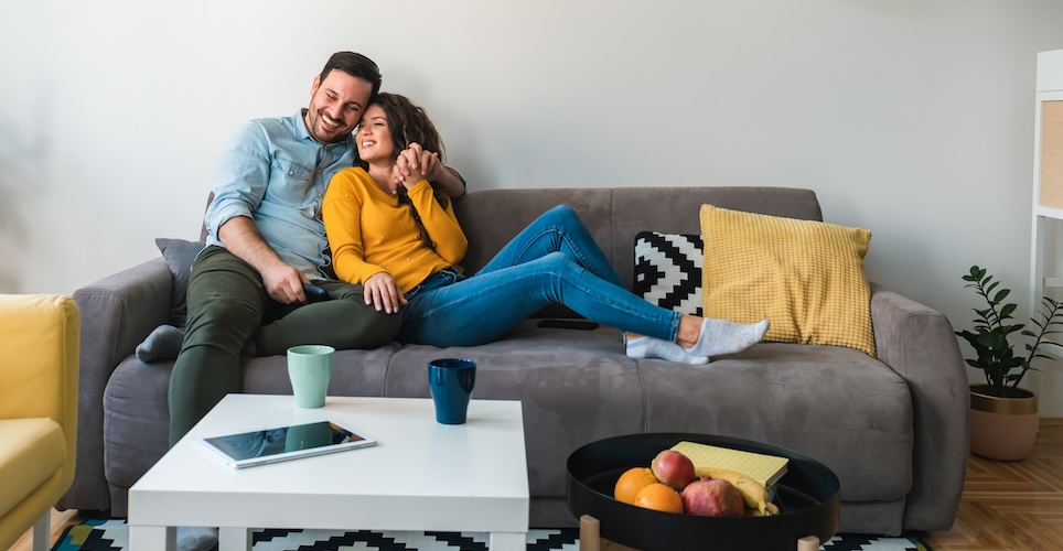 Couple sitting on couch talking, with a tablet visible and turned off on the table in the foreground. 