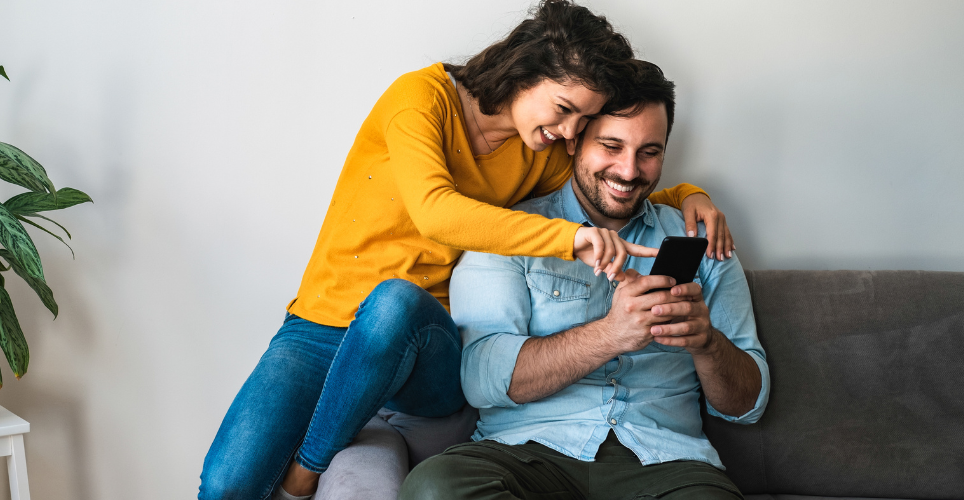 Couple sitting on couch looking at cellphone. 
