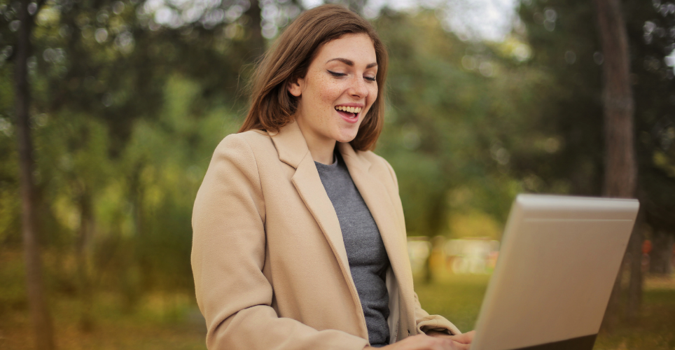 Smiling woman working on laptop outside.