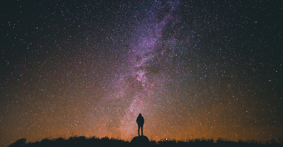 Far, abstract image of a tiny, silhouetted person against a colorful night sky