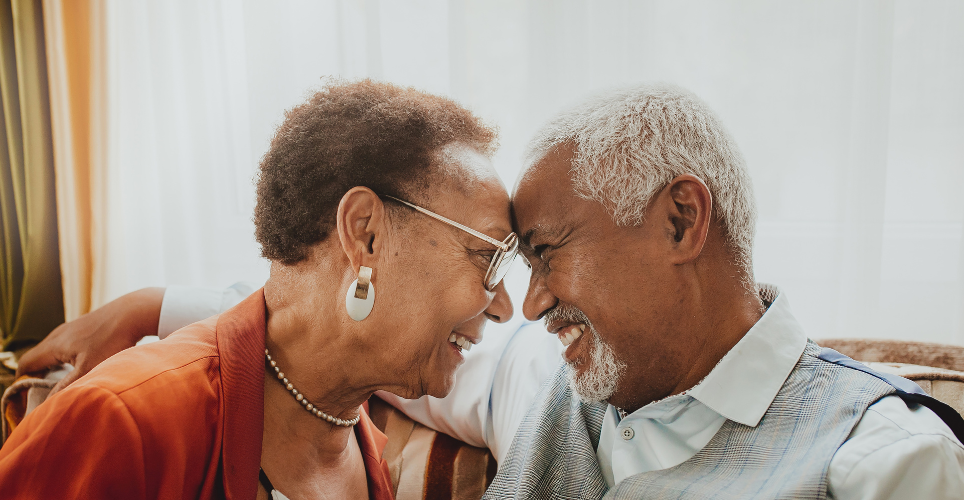 Older black couple looking at eachother smiling with foreheads touching.