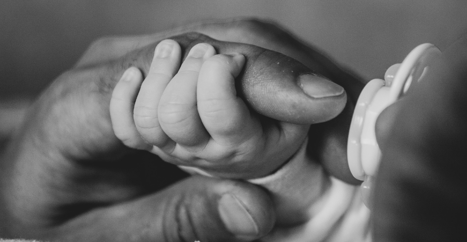 Newborn baby hand holding parents finger.