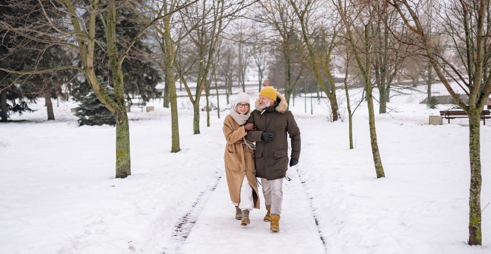 A distanced shot of an older, heterosexual couple walking on a snow-covered nature path.
