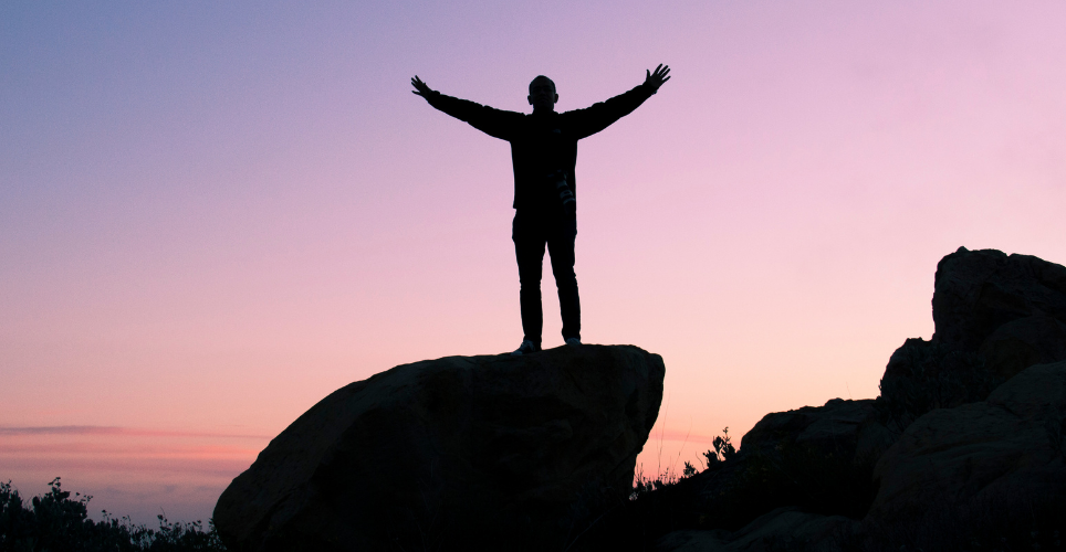 Man standing on rock with arms wide open during a sunset