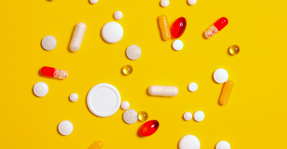 Colorful pills of different shapes on a bright yellow background.
