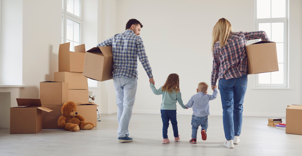 Family of four holding hands and boxes walking through house