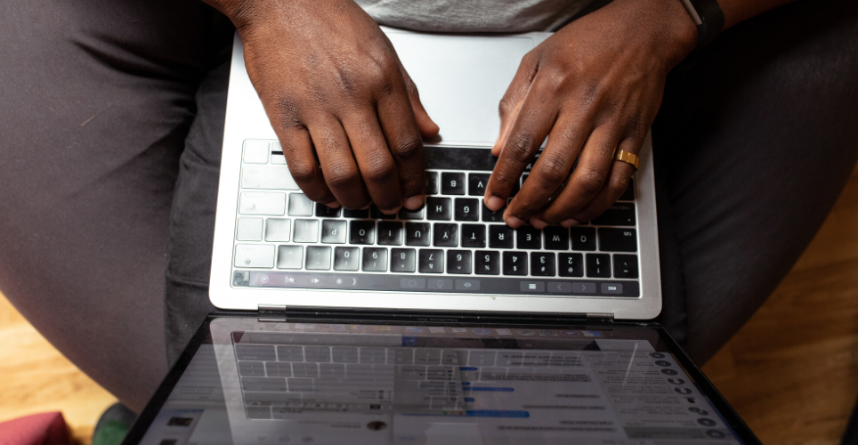 Close up of African-American hands on a black keyboard of a silver lap top.